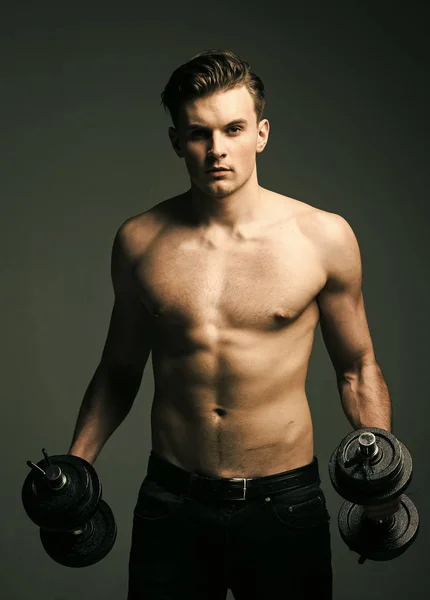 Training with dumbbells. Work out concept. Man with torso, muscular macho with six packs, holds dumbbells, dark background. Guy with tattoo attractive. Macho on confident face with muscular figure