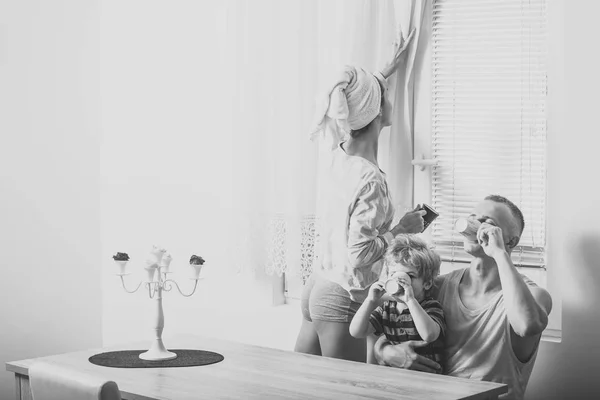 Семейное утро. Утренняя рутина. Мать, отец и ребенок сидят за столом утром. Счастливая семья проводит время вместе, белый интерьер и окно на заднем плане. Семья с улыбающимся чаем — стоковое фото