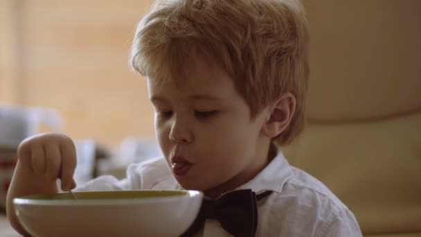 Gyermek eszik a kását a kanál és néz rajzfilmeket kis aranyos szőke fiú eszik a kását — Stock videók
