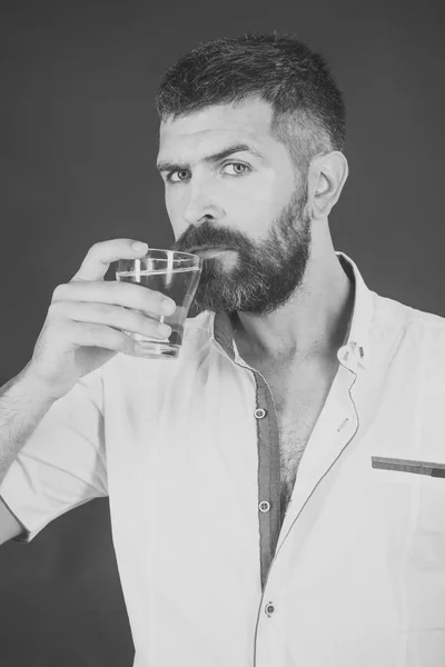 Hombre bebiendo agua. Hombre con barba larga sostiene el vaso de agua sobre fondo gris . —  Fotos de Stock