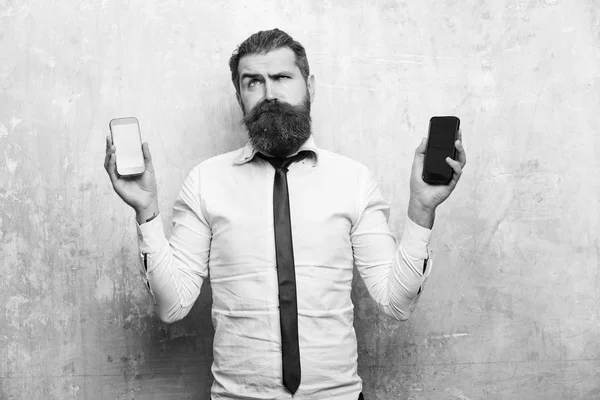 難しい選択。ヒップやひげを生やした男携帯電話とスマート フォンを比較します。 — ストック写真