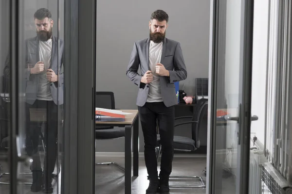 Stile di vita aziendale e d'ufficio. L'uomo barbuto guarda fuori dalla porta della stanza. Uomo d'affari in ufficio moderno con pareti in vetro. Uomo sicuro di se 'in giacca e cravatta sul posto di lavoro. Concetto di fiducia e successo — Foto Stock