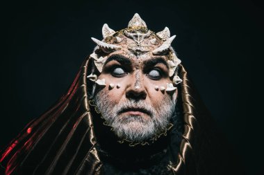 Kör sihirbaz metalik başlıklı sürpriz bakışla karanlık, büyü ve fantezi concept tarafından emilir. İblis kafa ile keskin dikenler ve siğiller siyah arka plan üzerine