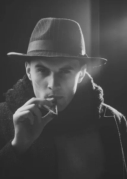 smoking person. Vintage detective concept. Man in coat, hat smoking cigar, dark background. Macho on mysterious face, detective, investigator, agent.
