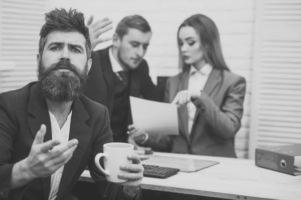 Litigi d'affari. L'uomo con la barba sul viso pieno di speranza tiene la tazza, i capi, i colleghi, i colleghi sullo sfondo. Concetto di negoziazione commerciale. L'uomo spera nel successo, in attesa che i partner discutano del contratto . — Foto Stock