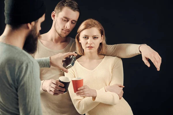 Amizade alcoólica. Homens, mulheres com rostos pensativos, fundo negro. Homens derramando xícara de mulheres com álcool fora do frasco. Conceção de bêbado. Companhia de amigos alegres fala e bebe . — Fotografia de Stock