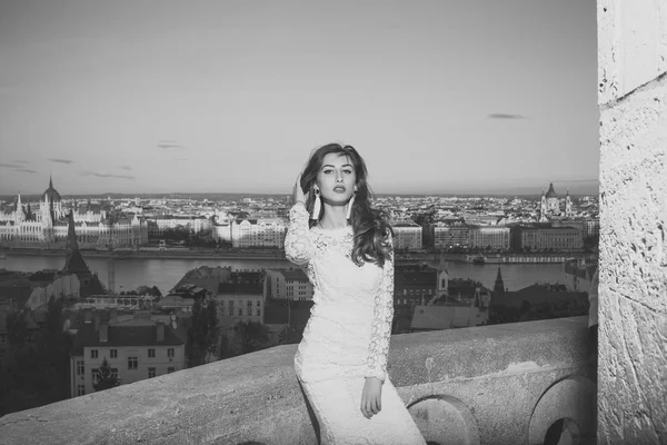 Μόδα μοντέλο πορτρέτο. Μόδα γυναίκα με μακριά μαλλιά στο μπαλκόνι, ομορφιά. Μόδα μοντέλο σε λευκό νυφικό για βράδυ με θέα στην πόλη — Φωτογραφία Αρχείου