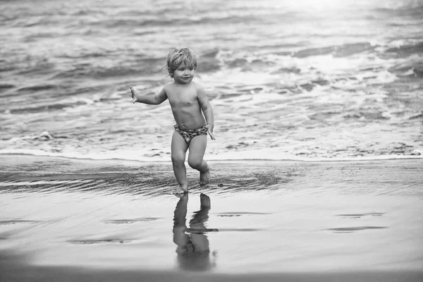 Kind op zee. Leuke vrolijke babyjongen loopt op natte zand langs de zee — Stockfoto