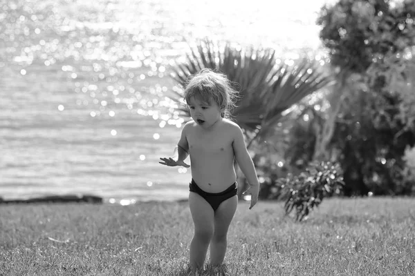 Ruhe auf dem Meer. Niedliche überrascht Baby Junge geht auf grünem Gras — Stockfoto