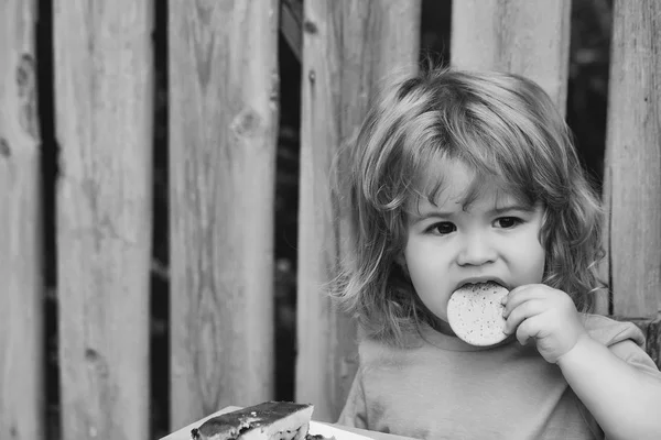 Kind eet op de natuur. kleine jongen eten taart in de buurt van houten hek — Stockfoto