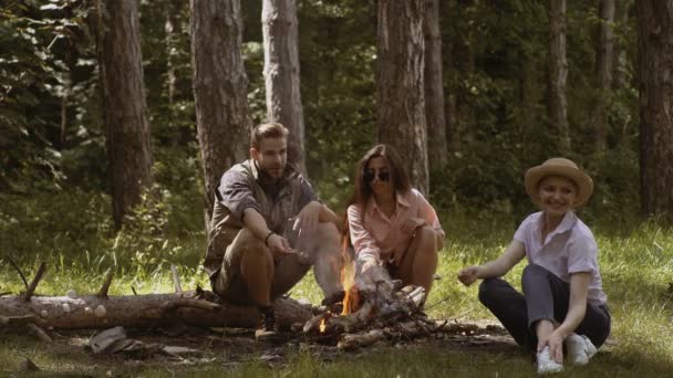 キャンプファイヤーでマシュマロを焙煎の友人のグループです。お友達と森で夕方火を甘いマシュマロを焙煎します。自然の中の焚き火を楽しんで幸せな友達。キャンプ友達のグループ — ストック動画