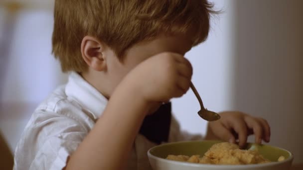 Menino feliz comendo mingau de cereal em si com colher — Vídeo de Stock