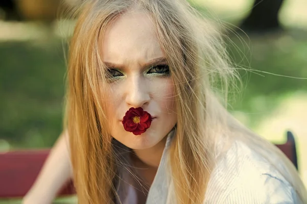Retrato de moda. Chica con cabello rubio y maquillaje sostienen flor roja en la boca de árbol en flor en primavera retrato al aire libre . —  Fotos de Stock
