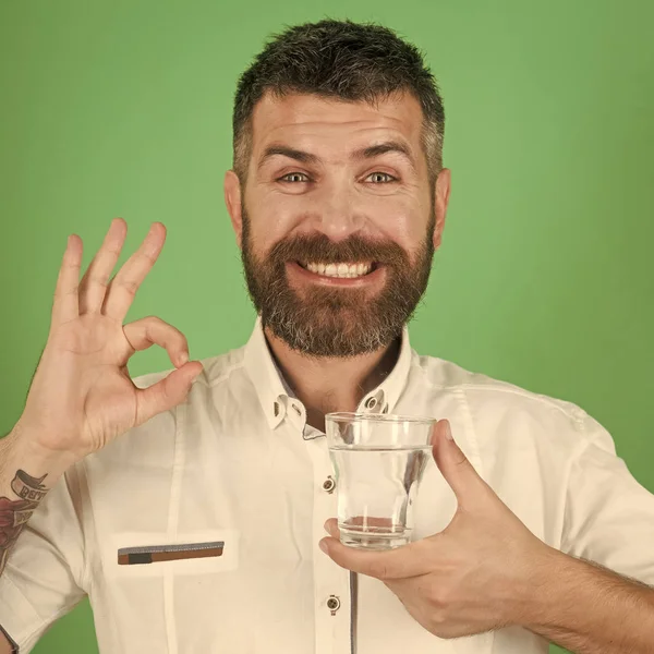 Mans health. Man with long beard hold water glass on green background.