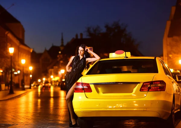 Девушка с гламурным макияжем. девушка в черном платье стоять у желтого автомобиля такси . — стоковое фото
