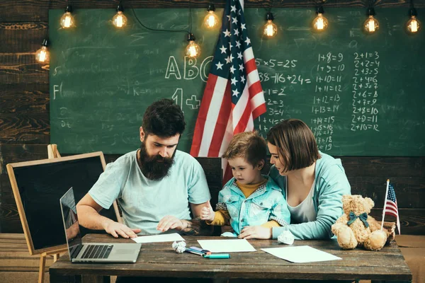 Dziecko z rodzicami w klasie z flagą usa, tablica na tle. Amerykańska rodzina siedzieć przy biurku z flagą syn i usa. Rodziców, uczy syna amerykańskiej tradycji gry. Koncepcja edukacji patriotycznej — Zdjęcie stockowe
