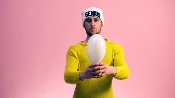 Il tipo in un maglione giallo con un cappello bianco su uno sfondo rosa fa clic su una grande lampada tra le mani. Concetto di idea . — Video Stock