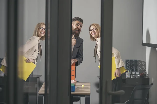 Des collègues heureux regardent dehors bureau moderne avec des murs en verre. Couple d'affaires sourire à la réunion. Homme barbu et femme sexy souriant avec des liants. Travailler ensemble sur le rapport. Concept de processus de travail — Photo