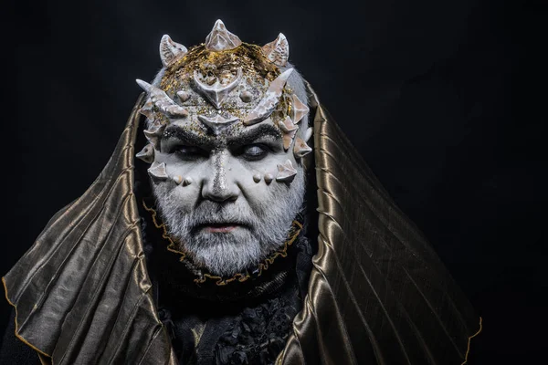 Man with thorns or warts, face covered with glitters. Demon with golden hood on black background. Senior man with white beard dressed like monster. Fantasy concept. Alien, demon, sorcerer makeup. — Stock Photo, Image