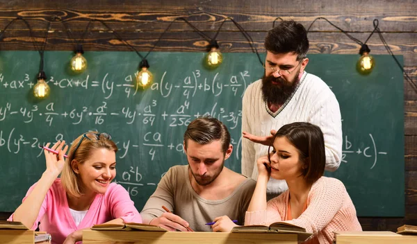 Estudiantes, compañeros de grupo hablando, pidiendo consejo, explica el profesor. Estudiar el concepto de dificultades. Profesor barbudo, profesor, profesor de enseñanza, pizarra en el fondo —  Fotos de Stock