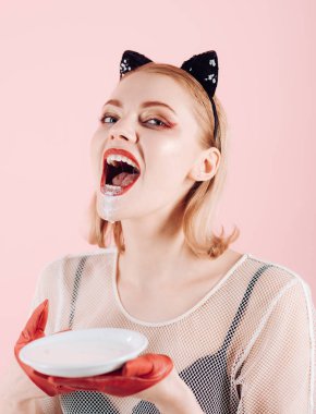 Kız yavru kedi kulakları ve yoğurt pembe bir arka plan üzerinde kırmızı eldivenler. kızla mutlu yüz süt İçecek.