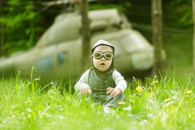 Çocuk ve doğal zemin üzerine bulanık helikopter. Oyun ve hayal. Mutlu çocukluk kavramı. Seyahat ve macera. Çocuk pilot kask ve yeşil çim oturan gözlük.