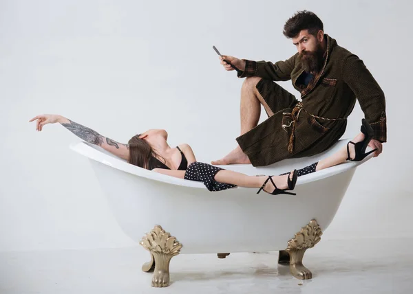 Skägg-konceptet. Man håller rakhyvel för rakning skägg. Man med orakad skägg ser på kvinnan avslappnande i badet. Beard grooming. Redo för morgon rakning — Stockfoto