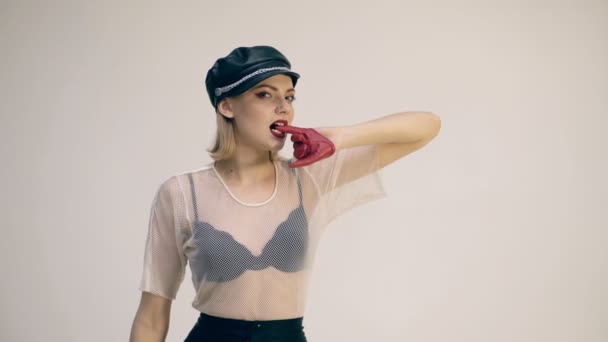 Modelo de niña en sombrero de cuero negro y guantes de cuero rojo sosteniendo el dedo en los dientes. Chica de moda. Concepto de moda . — Vídeos de Stock