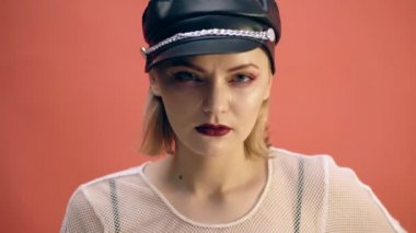 Kız siyah deri şapka ve kırmızı deri eldiven kırmızı bir arka plan üzerinde parmağını ısırır. Moda kavramı.