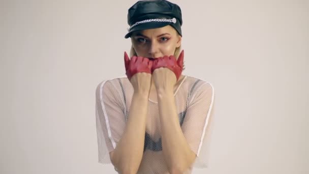 Concepto de chica gato. Una chica con un sombrero de cuero negro cubre su cara con sus manos usando guantes de cuero rojo . — Vídeos de Stock