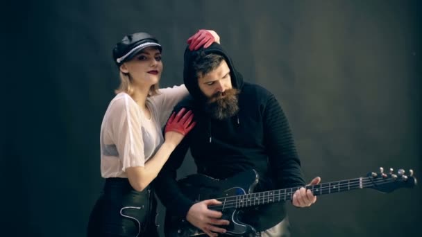 流行に敏感なひげを持つ男は、黒い背景に女の子の腕の中でギターを弾きます。ロッカー コンセプト. — ストック動画