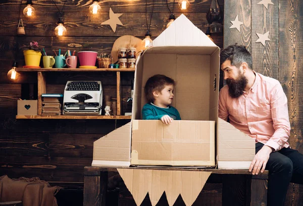 Kid happy sit in cardboard hand made rocket. Boy play with dad, father, little cosmonaut sit in rocket made out of cardboard box. Rocket launch concept. Child cute boy play cosmonaut or astronaut