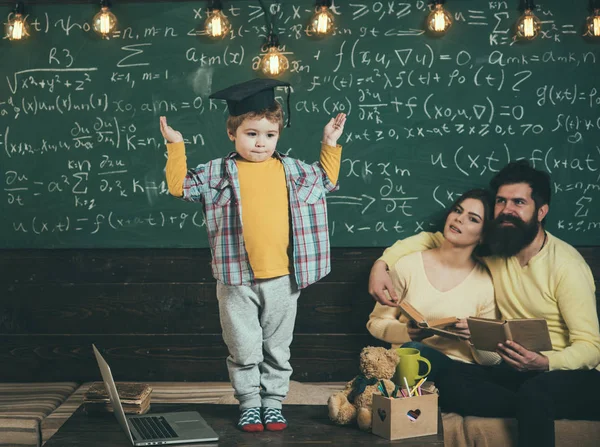 Studente rispondere lezione alla lavagna. Uno scolaretto con il berretto da laurea. Studente e famiglia in classe. Uomo e donna ascoltano lo scolaro. Conosco la risposta. — Foto Stock