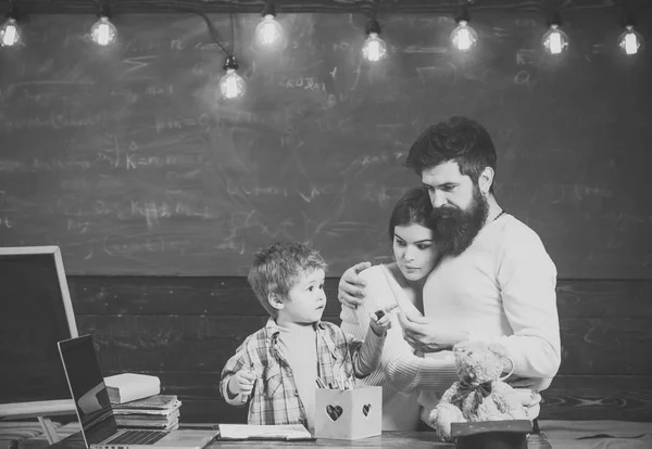 Περήφανοι γονείς βλέποντας γιους επιτυχία. Αγόρι στο πολυάσχολο πρόσωπο σχεδίου, ή γραπτώς. Γονική υποστήριξη έννοια. Γονείς βλέποντας ο γιος τους σχεδίασης, μαθαίνοντας να γράφουν, chalkboard σε φόντο. — Φωτογραφία Αρχείου