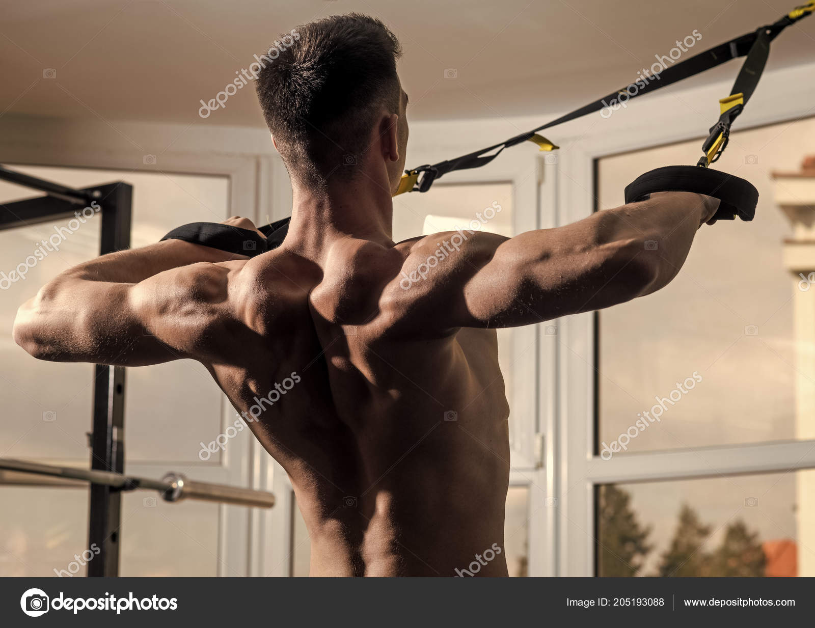 Sportsman, athlete, muscular macho does exercise with trx loops, window on  background, close up. Man with nude torso, and muscular back in gym enjoy  training, trx. Sport and gym concept Stock Photo