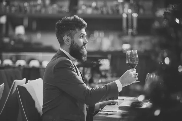 Passar um bom tempo no restaurante. Bonito jovem segurando copo com vinho tinto e sorrindo para o restaurante . — Fotografia de Stock