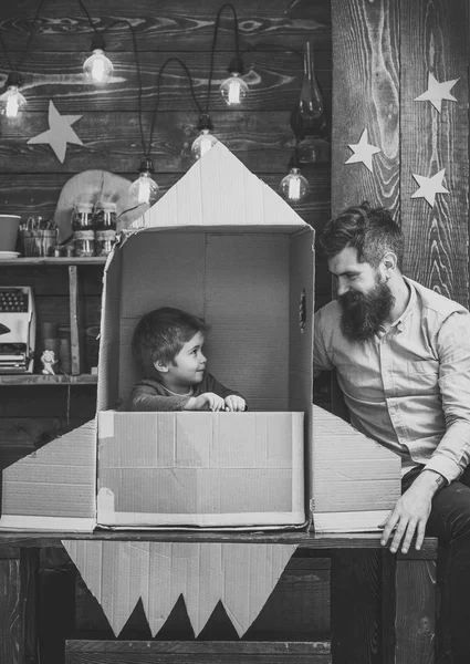 Kid happy sit in cardboard hand made rocket. Parenthood concept. Child cute boy play cosmonaut, astronaut. Boy play with dad, father, little cosmonaut sit in rocket made out of cardboard box — Stock Photo, Image