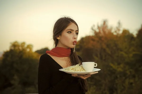 Beautiful woman eating pasta against natural background.