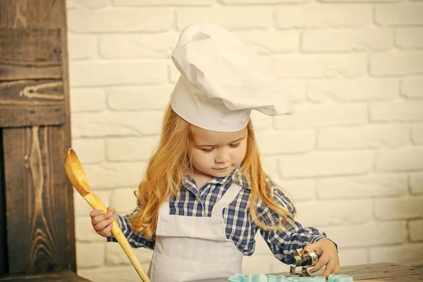 Child using spoon, rolling pin and cutters on table