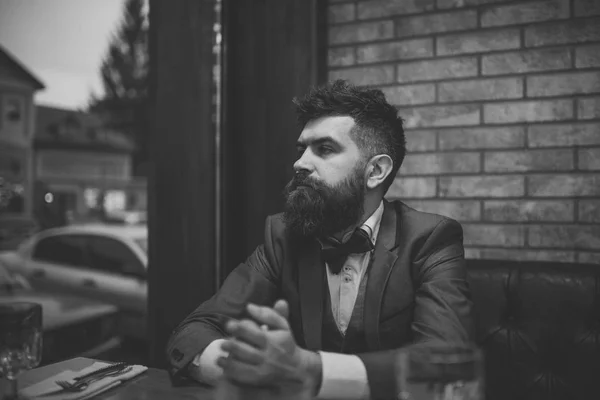 Confident bar customer sit in cafe and thinking. Date meeting of hipster awaiting in pub. Business on the go. Businessman with long beard in cigar club. Bearded man rest in restaurant