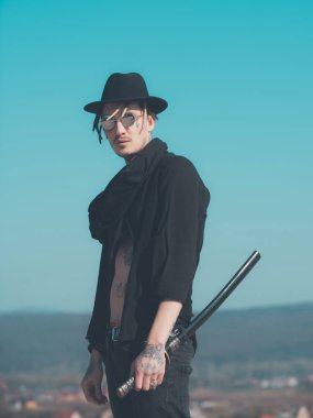 Savaşçı güneş gözlüğü, siyah şapka, açık giysili dövmeli gövde