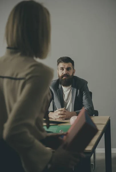 Retrato del socio de negocios sentado en el escritorio en la oficina con la mujer rubia asociada de pie delante de él —  Fotos de Stock