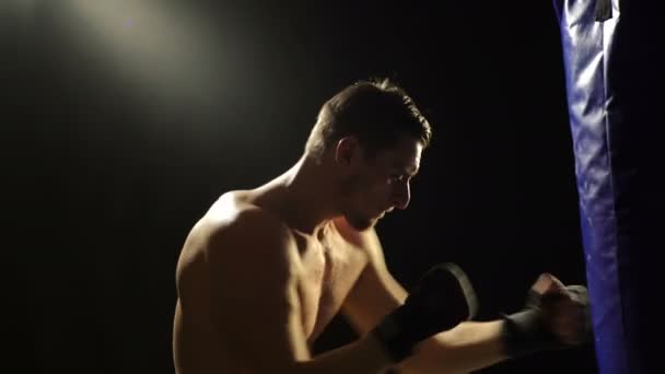 Концепция бокса. Боксер тренируется на голубой груше, изолированной на черном фоне. Сильный боксер на черном фоне . — стоковое видео