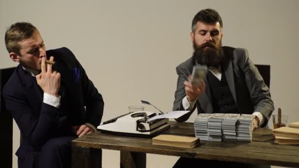 Концепція тіньового бізнесу. Два чоловіки в костюмах рахують гроші і курять сигари, сидячи за столом . — стокове відео