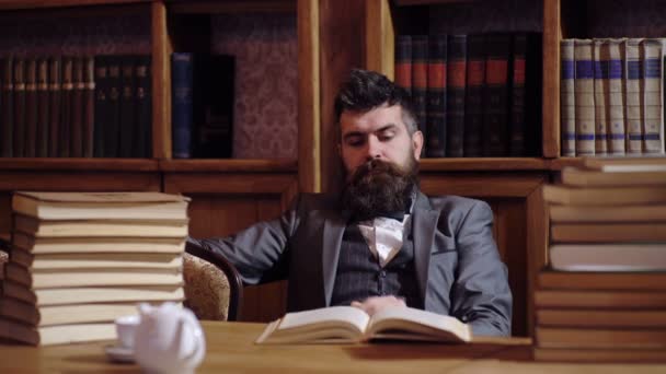 Un uomo barbuto pieno di libri in biblioteca legge un libro. Concetto di biblioteca. Il professore si prepara per una lezione in biblioteca . — Video Stock