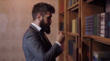 Sakallı bir adam bir kitaplık önünde duran bir okuma kitabı seçer. Kütüphane kavramı.