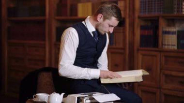 Bir adam bir kitaplıktaki bir masada oturan bir kitap okur. Profesör bir takım bilimsel malzeme Kütüphane çalışmaları.