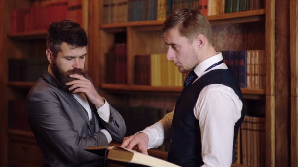 Deux hommes discutent à la bibliothèque tenant un livre entre leurs mains. Preuves scientifiques à la bibliothèque. Concept de travail scientifique . — Video