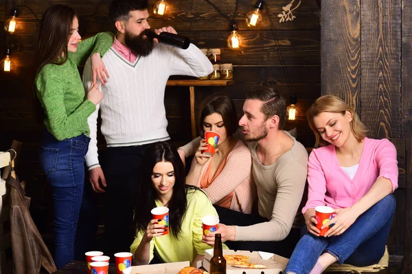 Students pizza party concept. Students, friends, group mates with teacher celebrate, have fun, dark wooden interior background. Youth celebrate with drinks and pizza, spend time together, speaking