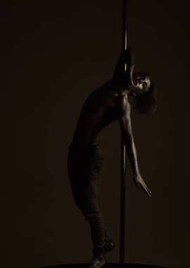 Metal yüzey ile seksi maço. Pole dans spor. Atletik erkekleri pilon üzerinde akrobatik öğeleri gösteriyor. Güçlü dansçı egzersiz kutup. Özgürlük. Kaslı adam pilon üzerinde dans gümüş beden sanatı ile.